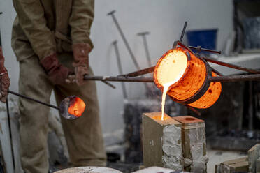 Handwerker gießen geschmolzene Bronze in einen Behälter in einer Gießerei - OCMF02128