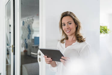 Lächelnde weibliche Fachkraft mit digitalem Tablet an der Kabine im Büro - DIGF15694