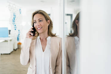 Businesswoman looking away while talking on smart phone by cabin in office - DIGF15696