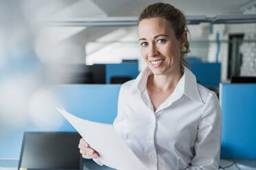 Smiling businesswoman with document standing in office - DIGF15707