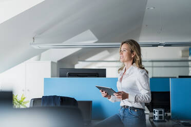 Geschäftsfrau schaut weg mit digitaler Tablet auf dem Schreibtisch im Büro sitzen - DIGF15709