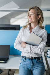 Smiling female entrepreneur with digital tablet leaning at desk - DIGF15711