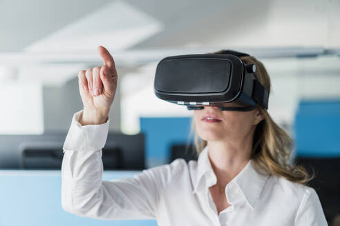 Geschäftsfrau gestikuliert bei der Verwendung eines Virtual-Reality-Headsets im Büro - DIGF15713