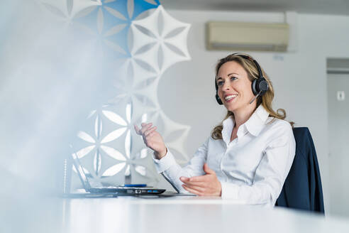 Female customer service representative gesturing while talking through headphones at desk - DIGF15717