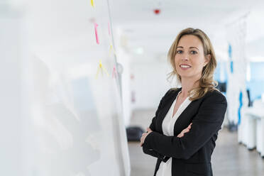 Businesswoman with arms crossed standing in front of whiteboard at office - DIGF15733