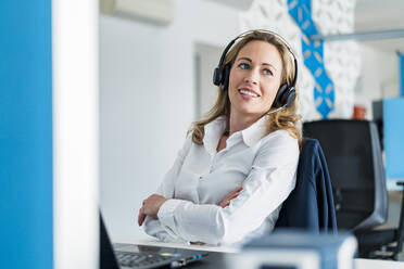 Female customer service representative with arms crossed sitting at desk - DIGF15754