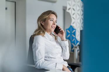 Businesswoman looking away while talking on mobile phone at office - DIGF15755