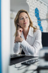 Thoughtful businesswoman looking away while sitting at desk in office - DIGF15756