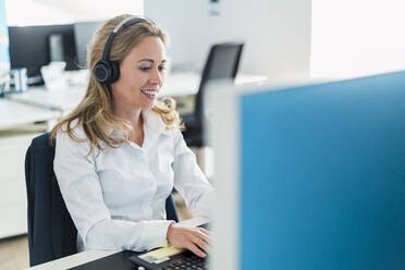 Lächelnde Kundendienstmitarbeiterin bei der Arbeit am Laptop im Büro - DIGF15758