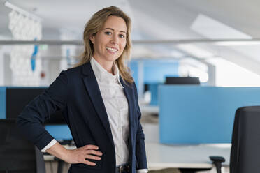Smiling female entrepreneur with hand on hip standing at office - DIGF15759