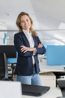 Female professional with arms crossed standing at office - DIGF15760