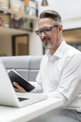 Lächelnder Geschäftsmann mit Laptop, der auf einen Laptop im Büro schaut - DIGF15775