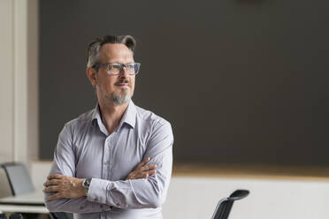 Thoughtful male entrepreneur with arms crossed looking away in office - DIGF15804