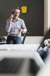 Älterer Geschäftsmann, der im Büro mit seinem Handy telefoniert - DIGF15806