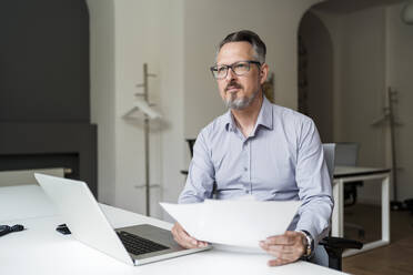 Geschäftsmann mit Laptop und Papierkram bei der Arbeit am Schreibtisch - DIGF15809