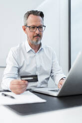 Männlicher Unternehmer mit Kreditkarte und Laptop im Büro - DIGF15828