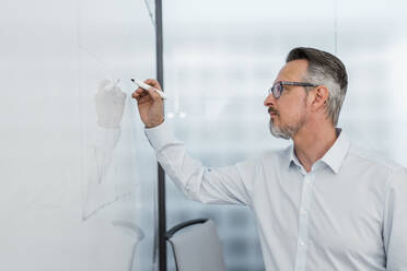 Businessman writing on whiteboard while working at office - DIGF15832