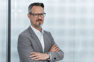 Confident businessman with arms crossed standing at office - DIGF15835