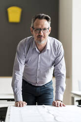 Businessman with blueprint leaning on desk at office - DIGF15863