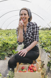 Lächelnde Bäuerin isst Erdbeeren auf einem landwirtschaftlichen Feld - JRVF00917