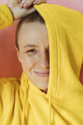 Junge Frau bedeckt halbes Gesicht mit Kapuzenpulli im Studio - VPIF04156