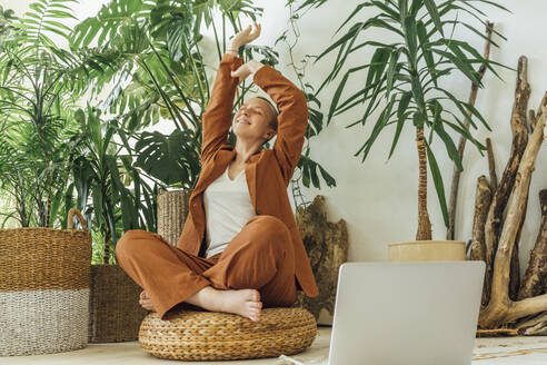 Female entrepreneur stretching arms by laptop in office - VPIF04171