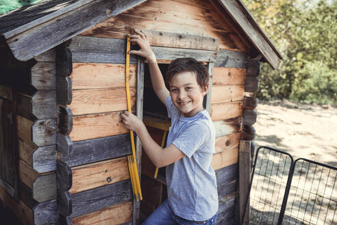 Smiling boy measuring wooden rabbit hutch with tool in back yard - HMEF01269