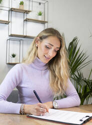 Female professional with blond hair signing documents in office - JCCMF02687
