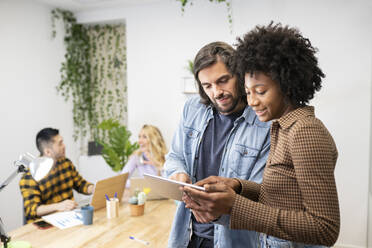 Businesswoman explaining strategy over tablet to male colleague in office - JCCMF02695