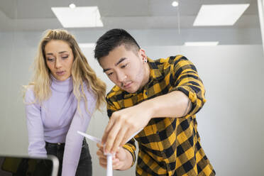 Young male professional adjusting wind turbine while standing by female colleague in office - JCCMF02715