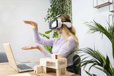 Junge weibliche Fachkraft, die einen Virtual-Reality-Simulator trägt, gestikuliert bei einem Videoanruf im Büro - JCCMF02728