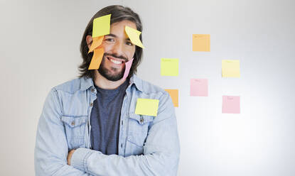 Smiling male professional standing with adhesive notes sticking on face - JCCMF02732