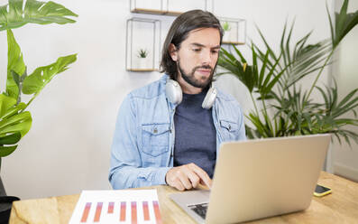 Businessman using laptop while sitting at desk in office - JCCMF02759