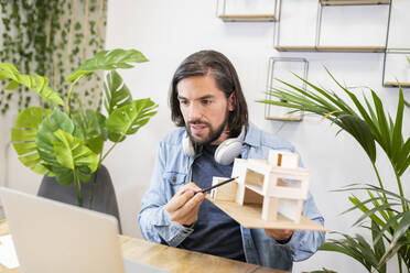 Männlicher Unternehmer mit langen Haaren, der ein Architekturmodell per Videoanruf im Büro erklärt - JCCMF02764