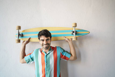 Happy handsome man with longboard in front of wall - RCPF01137
