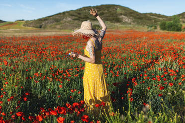 Mittlere erwachsene Frau inmitten von roten Mohnblumen an einem sonnigen Tag - MRRF01197