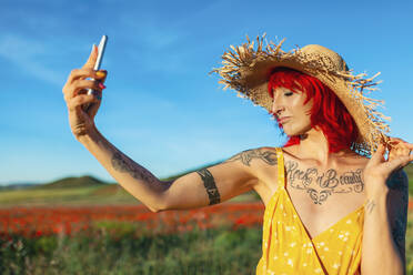 Frau mit geschlossenen Augen nimmt Selfie durch Smartphone an sonnigem Tag - MRRF01218