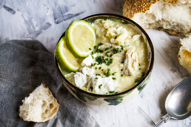 Schüssel mit griechischer Avgolemono-Suppe mit Reis, Zitronenscheiben und Brot - SBDF04472