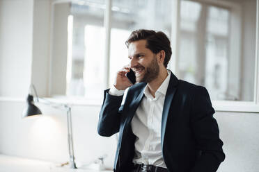 Smiling businessman talking on smart phone at office - GUSF05953