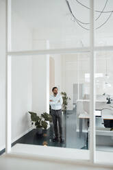 Male entrepreneur with arms crossed standing in office - GUSF05961