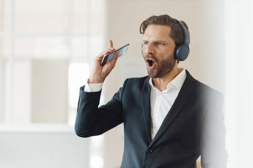 Businessman with smart phone listening music through headphones at office - GUSF05974