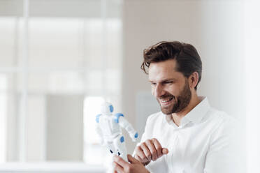 Lächelnder Geschäftsmann hält Robotermodell im Büro - GUSF05980