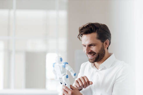 Smiling businessman holding robot model in office - GUSF05980