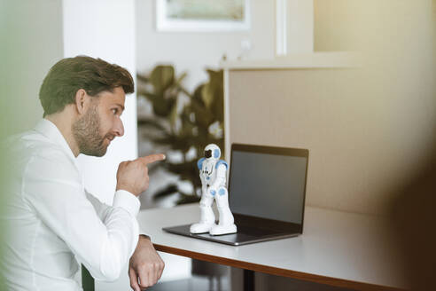 Male entrepreneur pointing at robot on laptop at office - GUSF05985