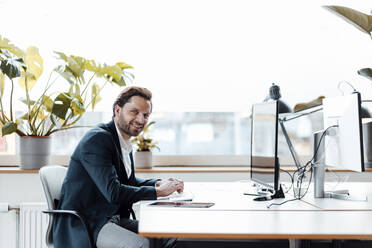 Smiling businessman sitting by desk at office - GUSF05990