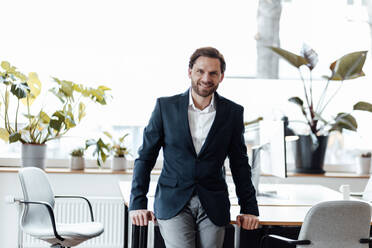 Smiling businessman leaning on desk at office - GUSF06001