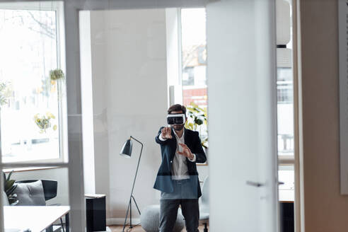 Businessman with virtual reality headset stretching hand while standing in office - GUSF06006