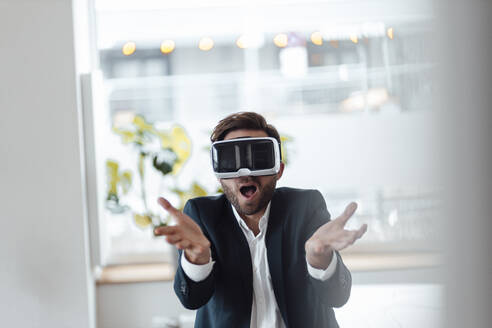 Geschäftsmann mit offenem Mund, der ein Virtual-Reality-Headset im Büro benutzt - GUSF06007