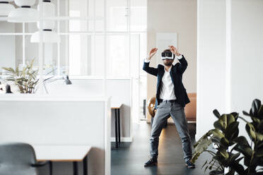 Businessman stretching hands while using virtual reality headset in office - GUSF06009