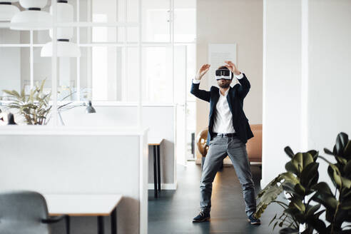 Geschäftsmann streckt die Hände aus, während er ein Virtual-Reality-Headset im Büro benutzt - GUSF06009
